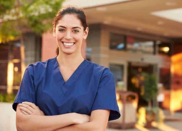 A woman in scrubs standing outside of a building.